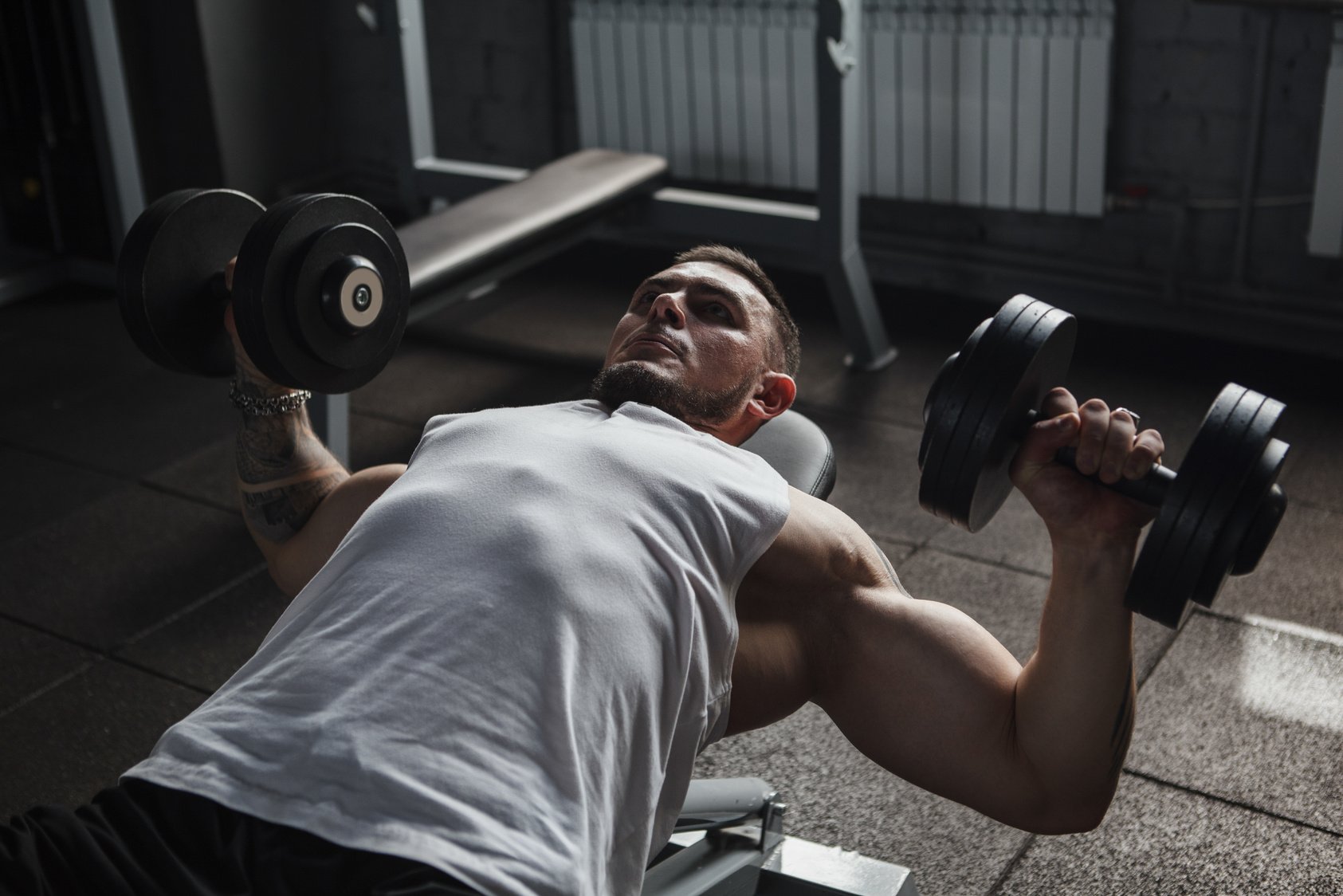 Strong muscular sportsman doing dumbbells chest press exercise